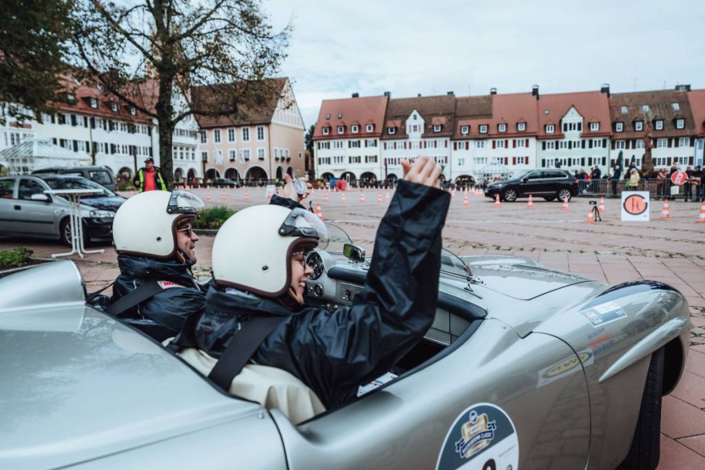 A course is set up for the event on the market square in Baiersbronn. A couple drive onto the market square in a silver open-top vintage car and wave to the spectators.