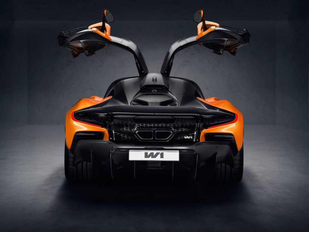 Man sieht eine Studioaufnahme des MacLaren W1 von hinten mit nach oben geöffneten Flügeln. Das Cabrio ist in den Farben Titanschwarz und Orange lackiert. Auf dem Nummernschild steht "W1". Hintergrund, Wände und Boden sind ebenfalls schwarz.
