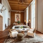 Die große Empfangshalle in warmen Braun-, Weiß- und Goldtönen bietet einen majestätischen Eindruck. An den Wänden hängen Geweihe und von der Decke große Lüster. Die Sessel sind mit weißen Fellen bedeckt.