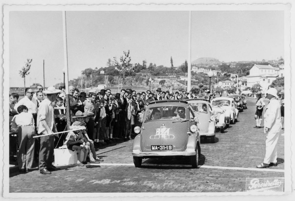 The black-and-white image shows several vintage cars crossing a finish line one after the other.