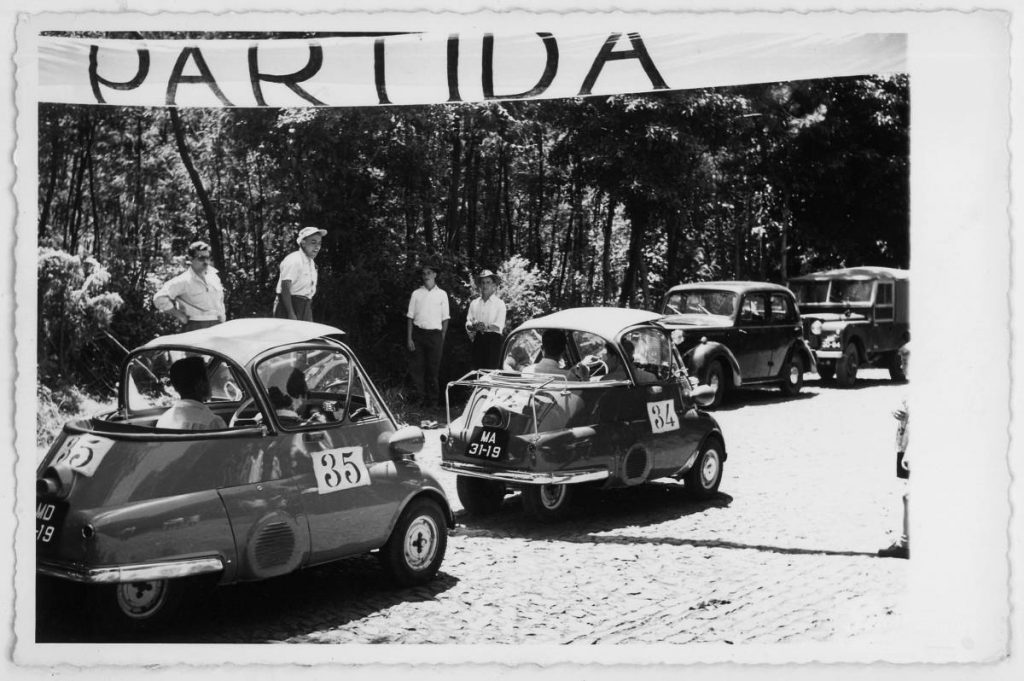 Two Isettas with start numbers 34 and 35 at a car rally. Above you can see a banner with the inscription "Partida".