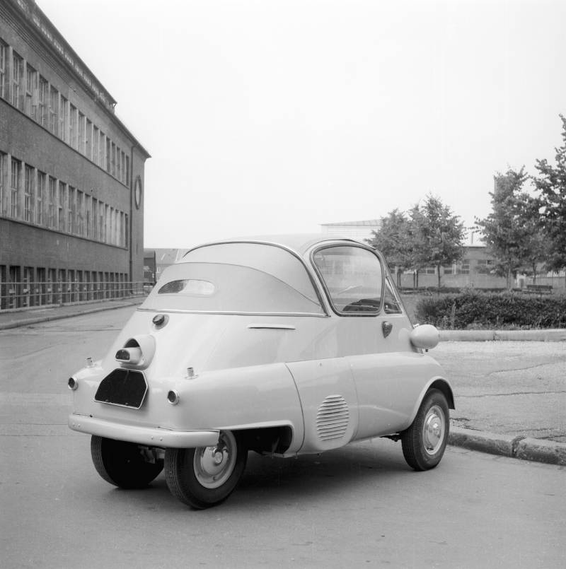 A black and white picture with a white Isetta convertible. The car is parked in front of a building.