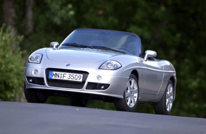You can see a silver Fiat Barchetta convertible at an angle from the front with the roof open.