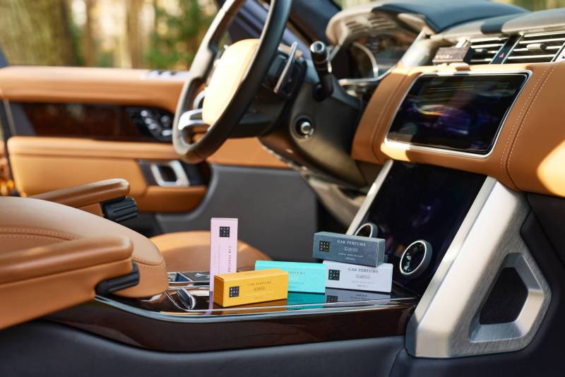 Es ist das Interieur des Cockpits eines edlen Cabrios zu sehen: Auf dem Beifahrersitz liegen bunte Schachteln mit verschiedenen Auto-Parfums für den Car Diffuser zu sehen. Das Bild ist in warmen Beige- und Brauntönen gehalten.