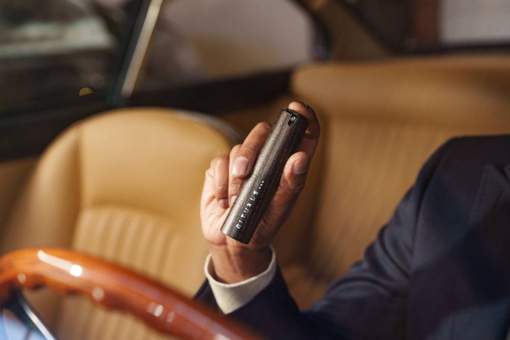 Ein Mann in einem edlen Cabrio mit hellbraunen Ledersitzen hält einen Car Diffuser von "Rituals" in der Hand.