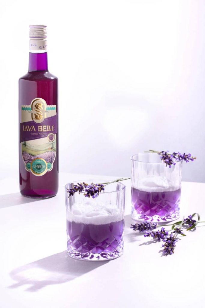 Lav'a Belle Nizza Mule alkoholfrei – eine lilafarbene Flasche, zwei Gläser mit dem lilafarbenen Drink und Lavendel als Garnitur