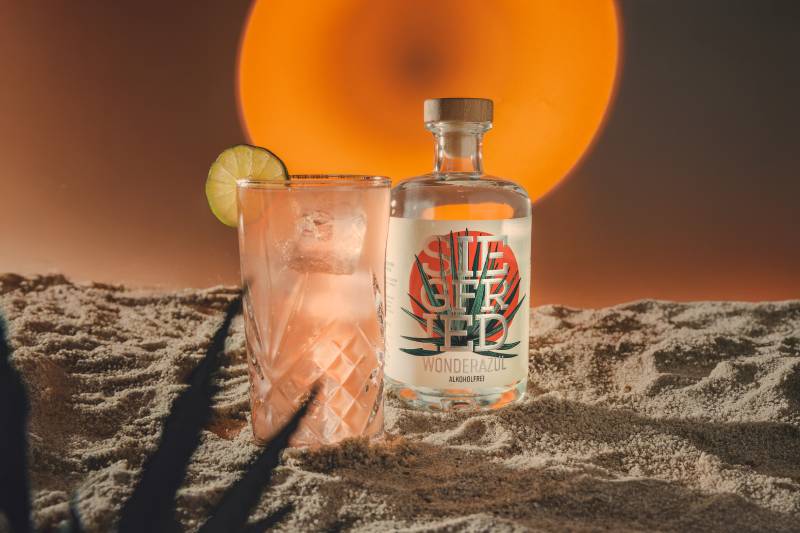 Wonderazul alkoholfrei in einer stylischen Flasche mit der Aufschrift "Siegfried" neben einem Glas mit Eiswürfeln und einer Limettenscheibe.