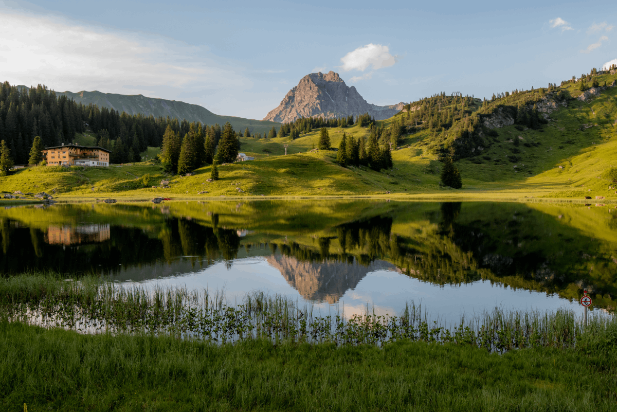 Cabriolife on Tour: Man sieht den Großen Widderstein, einen markant aufragenden Berg in den Lechtaler Alpen. Im Vordergrund liegt ein kleiner stiller See, in dem sich der Berg spiegelt. Das Bild ist in satten Grüntönen gehalten.