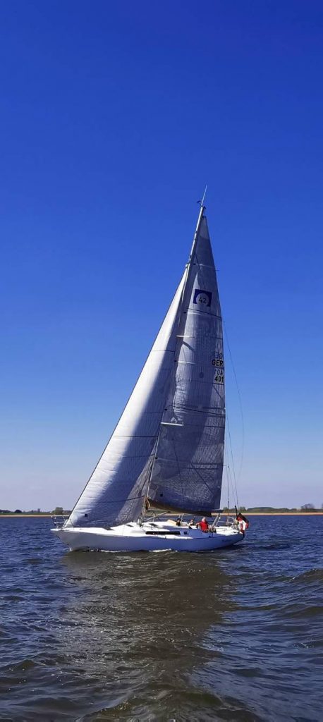 Omega 42 vom schwedischen Yacht-Designer Peter Norlin gilt als Ikone des Bootsbaus – vergleichbar mit dem Status eines Jaguar E-Type oder Mercedes SL Roadster. Auf dem Bild mit stahlblauem Himmel sieht man das Boot mit voll gesetzten Segeln.